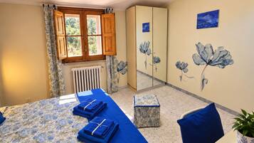 Una habitación con cama, armario, radiador, ventana con cortinas y un cuadro floral en la pared.