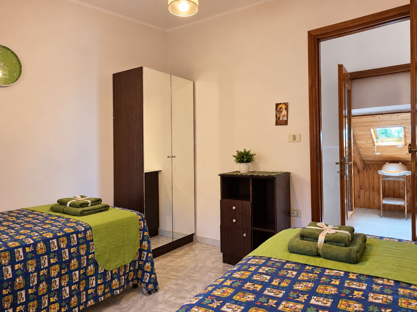 Een slaapkamer met twee bedden, een kledingkast, een klein kastje en een deur naar een balkon.