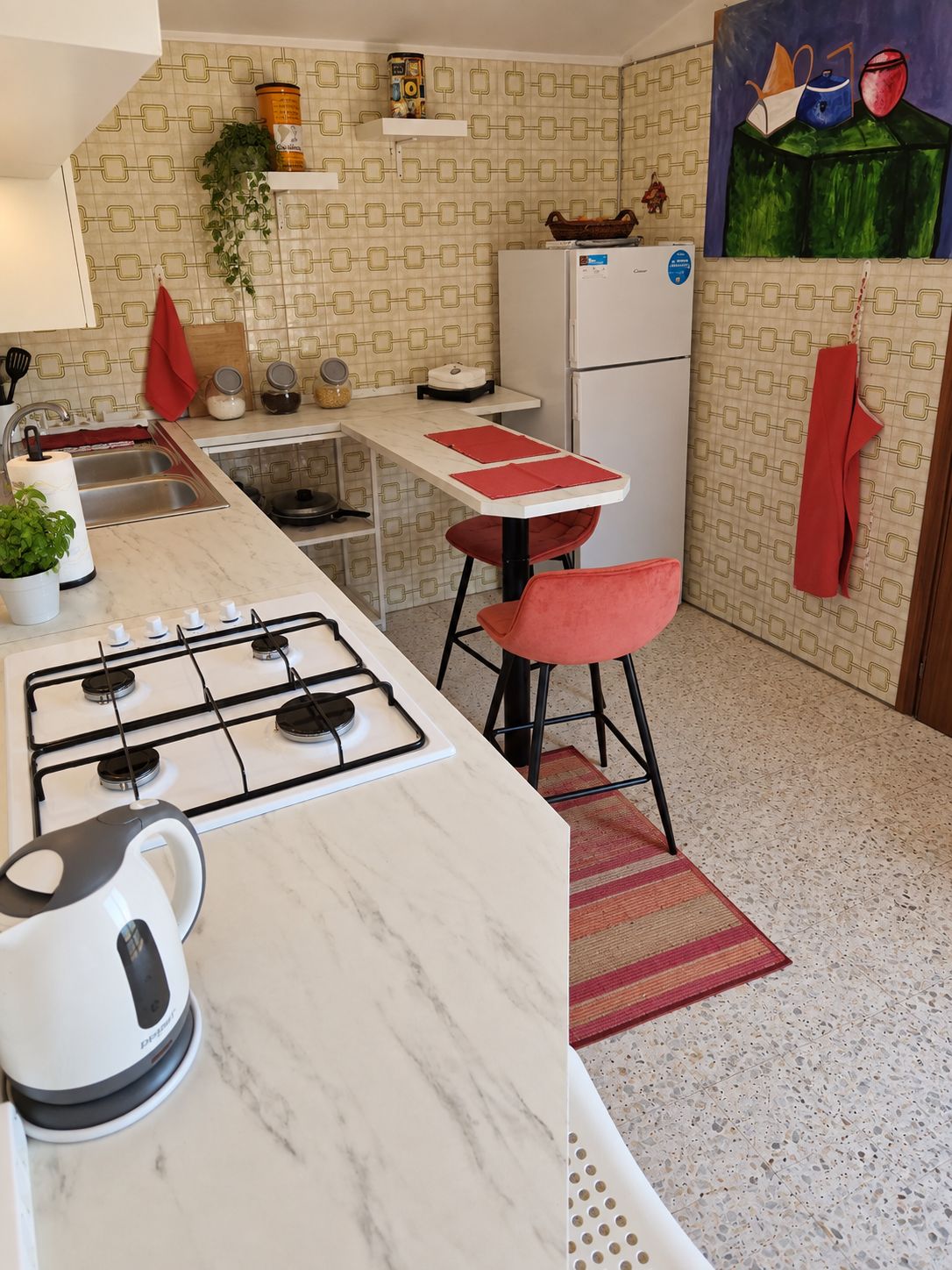 A compact kitchen with a gas stove, a refrigerator, and a small dining area with stools.
