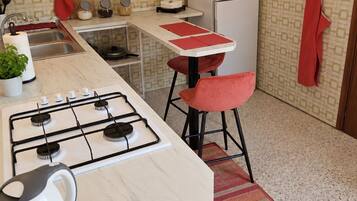 A compact kitchen with a gas stove, a refrigerator, and a small dining area with stools.