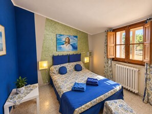 A bedroom with a bed, bedside lamps, a radiator, a window with curtains, and a painting on the wall.