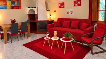 A living room with a red sofa, a fireplace, a dining area with a table and chairs, and a red rug.