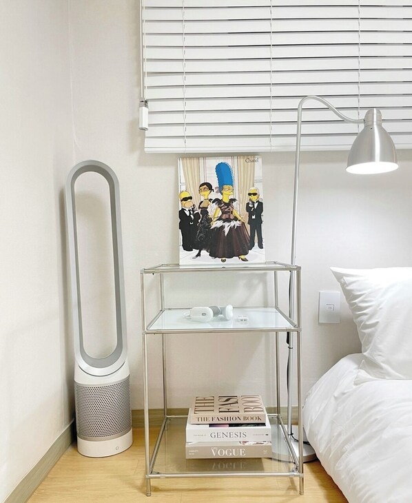 A neatly arranged bedroom with a bedside table holding a lamp, a speaker, and a stack of books.
