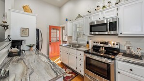 A modern kitchen with white cabinets, stainless steel appliances, and a marble countertop.