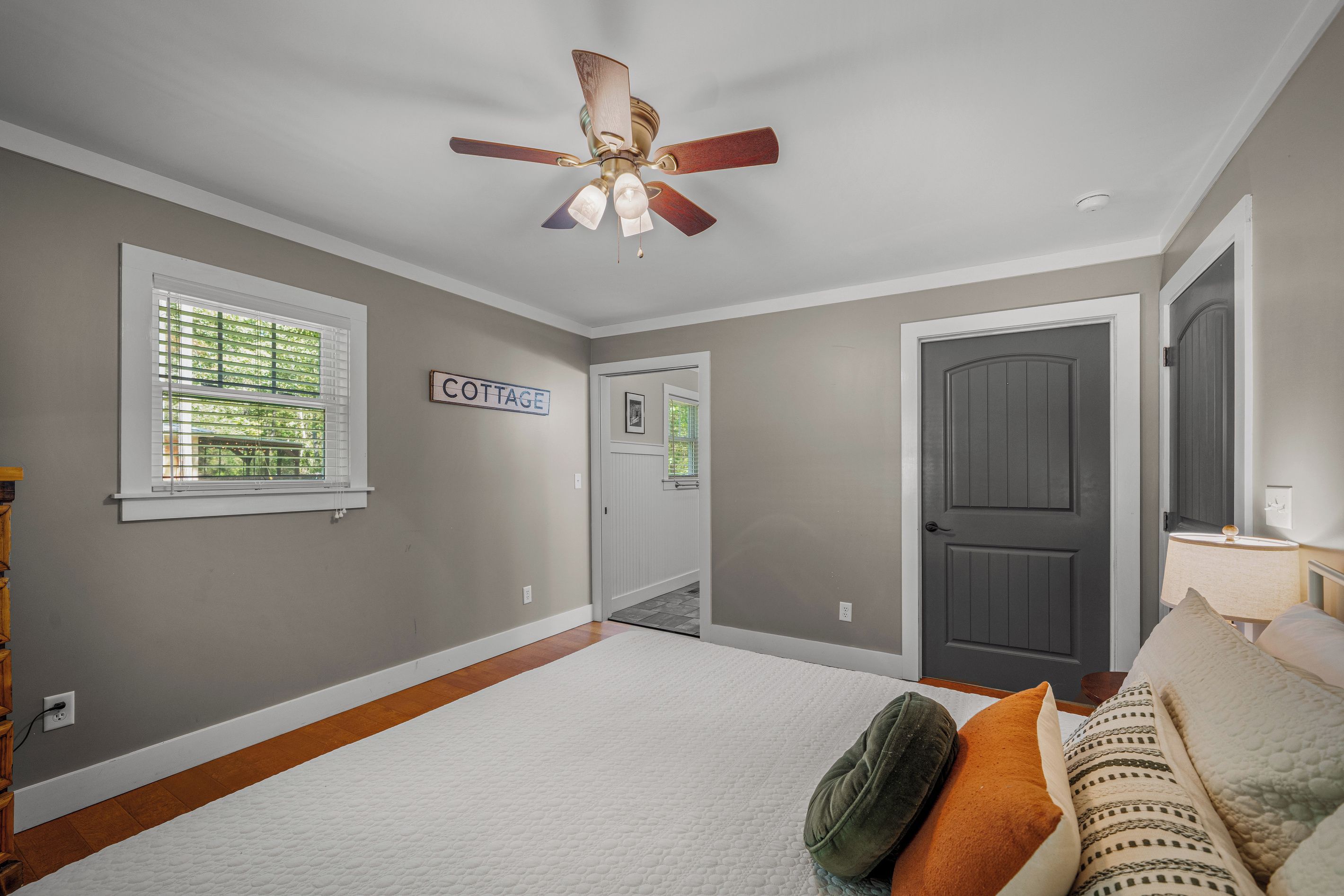 A room with a ceiling fan, a door labeled 'COTTAGE', and a window with blinds.