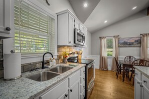 A modern kitchen with granite countertops, stainless steel appliances, and a dining area with wooden chairs.