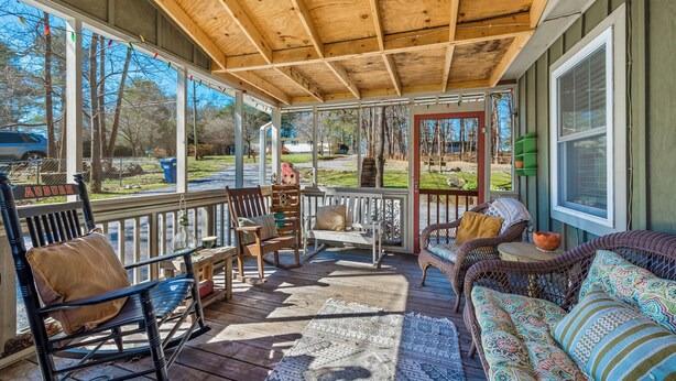 A covered porch with wooden flooring, a cushioned bench, a wicker sofa, and a view of the surrounding landscape.