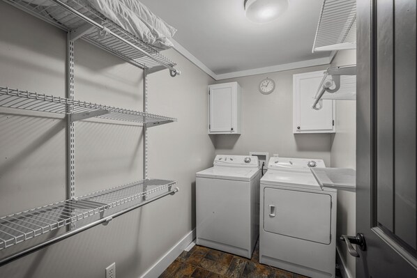 A laundry room with two stacked washers and dryers, metal shelving units, and a clock on the wall.