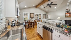 A kitchen with a dining area, wooden ceiling beams, and recessed lighting.