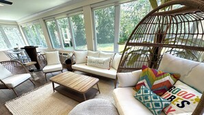 Ein helles Wohnzimmer mit einer Couch, Sesseln, einem Couchtisch und einem Korbstuhl.