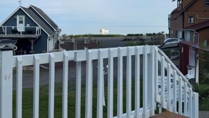 A wooden deck with a white picket fence, a grassy yard, and a view of a distant boat on the water. - Tide’s Edge Escape: Cozy 2-Bed Cottage/Camper with Sea Views  (Orange Hill)