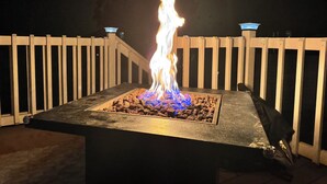 A fire feature with a square stone base, surrounded by a wooden deck. - Tide’s Edge Escape: Cozy 2-Bed Cottage/Camper with Sea Views  (Orange Hill)