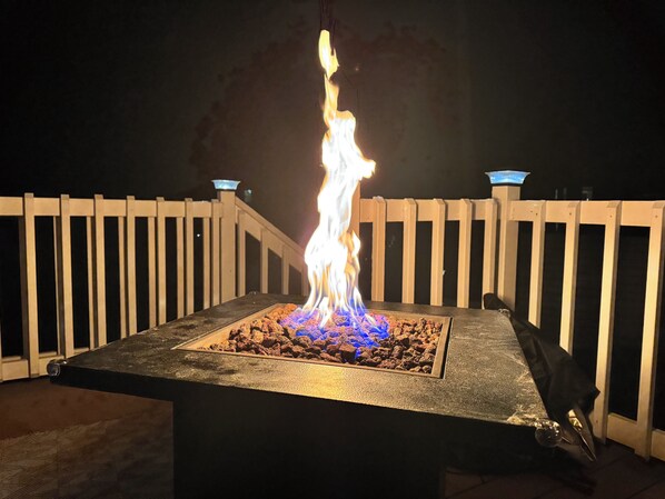 Un foyer dont la base est constituée d’une structure carrée en pierre, entouré d’une terrasse en bois.