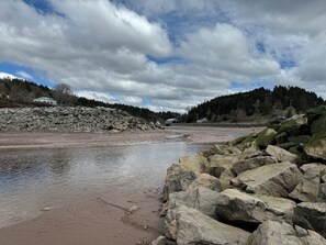 Una costa rocosa con un río, una casa y una colina boscosa al fondo.