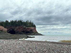 Une côte rocheuse avec l’entrée d’une grotte, une forêt dense et un ciel nuageux.