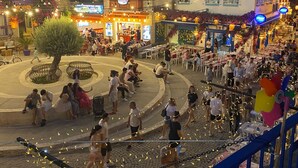 A bustling square with outdoor seating, a central tree, and various shops and restaurants. - Meydan otel (Cesme)