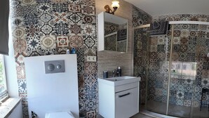 A bathroom with a white toilet, a sink with a mirror, and a shower area with patterned tiles. - Meydan otel (Cesme)