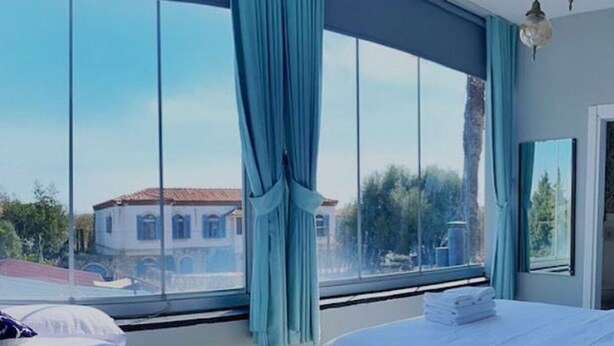 A bedroom with a large window, a bed, and a view of a building outside. - Meydan otel (Cesme)