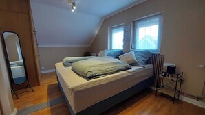 Un dormitorio con una cama, una mesita de noche, un espejo y una ventana.