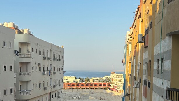 A view of a residential area with multi-story buildings, a swimming pool, and a beach in the background. - Wake up looking at the Red Sea! (Hurghada)