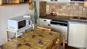 Eine kleine Küche mit Holzregalen, einer Mikrowelle, einem Herd und einem Tisch mit Tischdecke.