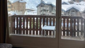 Ein Zimmer mit Holzbalkendecke, einem Balkon mit Holzgeländer und Blick auf schneebedeckte Gebäude und Berge.