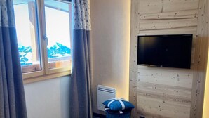 A hotel room with a bed, a TV mounted on the wall, a window with curtains, and a radiator.