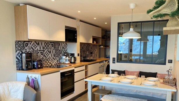 A modern kitchen with white cabinets, patterned backsplash, and a dining area with a table set for four.