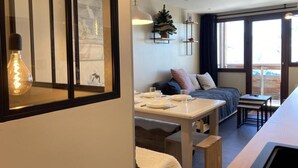 A cozy room with a dining table set for two, a sofa, and a small bed. There is a window with a view of the outdoors.