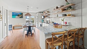 A modern kitchen with white cabinetry, wooden shelves, and a marble island. - Sea Bound, Private Pool, Fire Pit, Multiple Decks, Hot Tub- 2 Blocks To Beach (Gulf Shores)