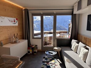 Una stanza accogliente con parete in legno, un divano, un tavolino e vista sulle montagne innevate attraverso ampie finestre.