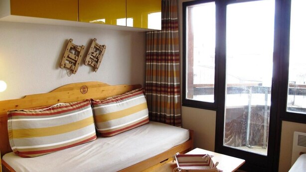 A cozy room with a wooden bed, striped pillows, a small table with books, and a window with curtains. - 10m from ski slopes, 3rd floor, tv, ski locker, 21m², Avoriaz (Avoriaz)