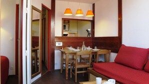 Une pièce de taille modeste comprenant une table à manger, des chaises, un canapé rouge et une petite kitchenette.