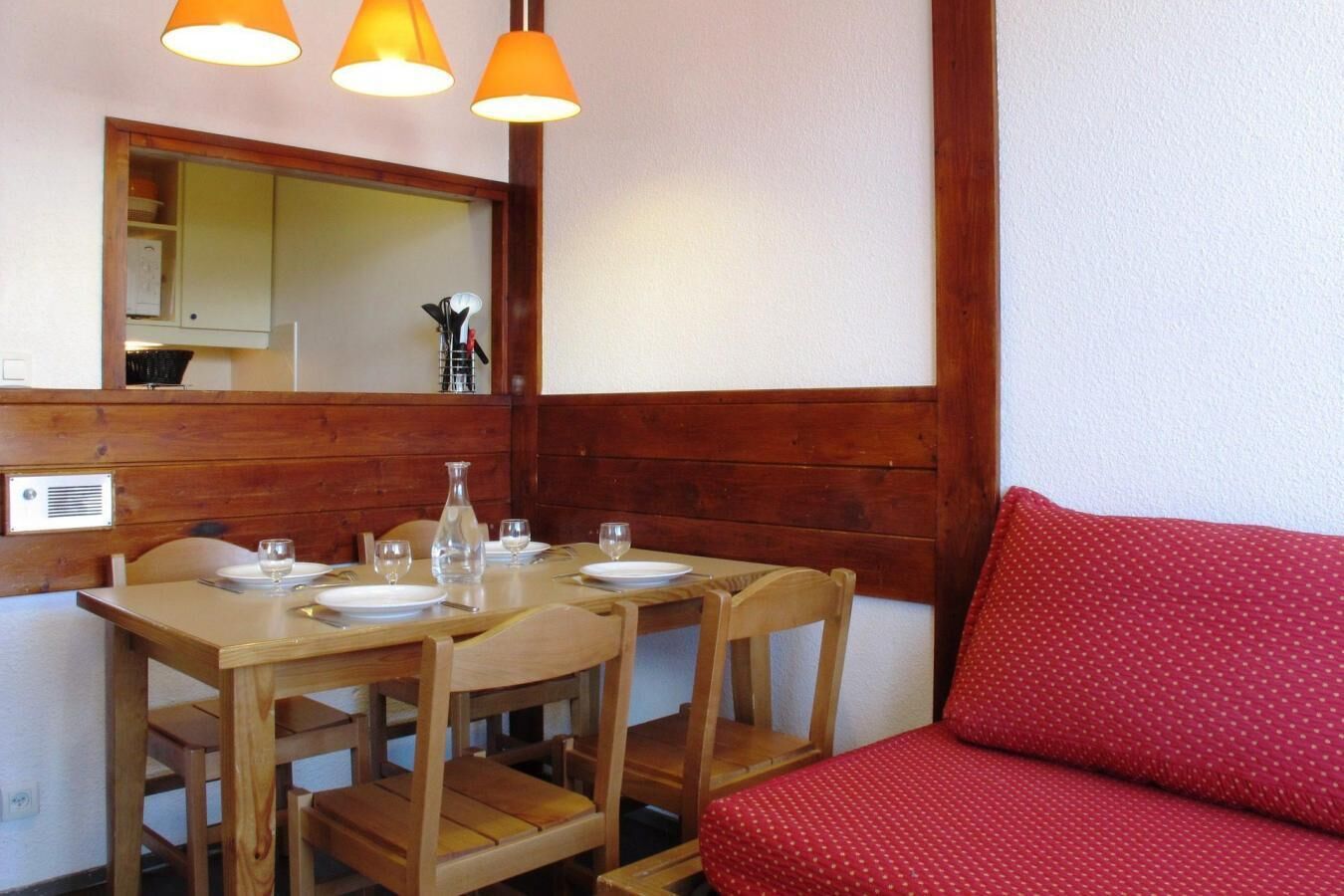 Un comedor con una mesa de madera dispuesta para dos personas, dos sillas y un sofá rojo.