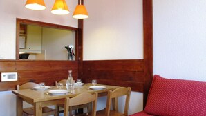 Un coin repas avec une table en bois dressée pour deux personnes, deux chaises et un canapé rouge.