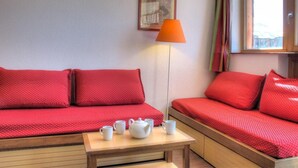 Une pièce avec deux canapés rouges, une table avec une théière et des tasses, une lampe et un tableau encadré au mur.