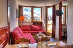 A cozy room with a wooden table set for dining, a red sofa with cushions, a window with a mountain view, and a television mounted on the wall. - 10m from ski slopes, 3rd floor, view resort, balcony, tv, ski locker, 26m², Avoriaz (Avoriaz)