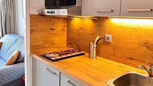 Eine kompakte Küchenzeile mit Mikrowelle, einer Holzausziehtheke, einem Spülbecken und einer kleinen Essecke mit Tisch und Stuhl.