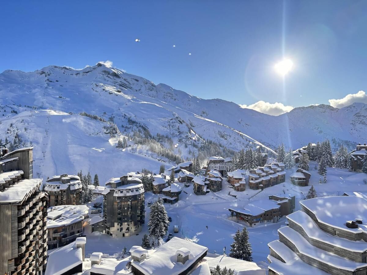 Ein verschneites Bergdorf mit traditionellen Chalets, einer Skipiste und blauem Himmel.