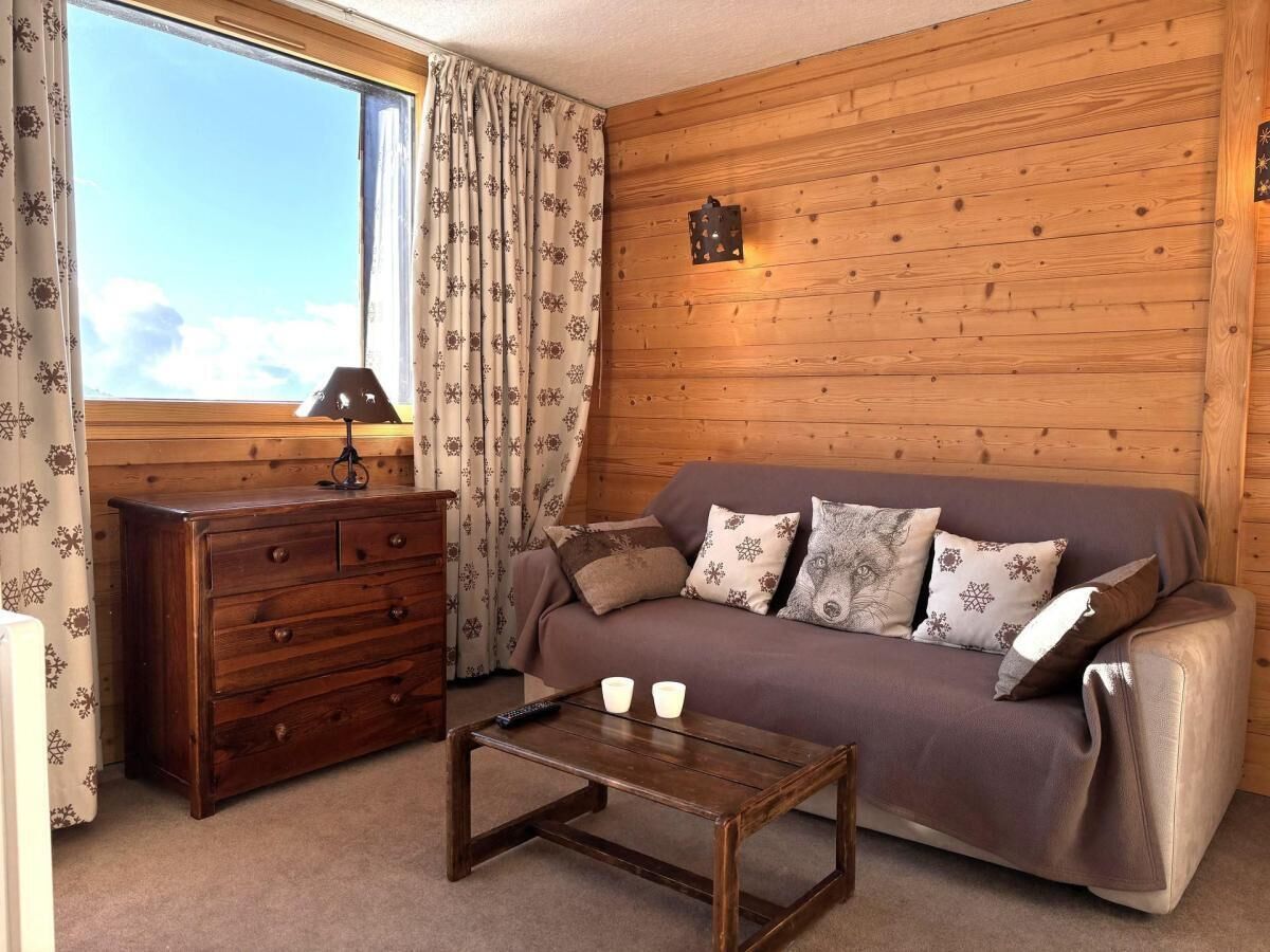 Una habitación acogedora con pared de madera, un sofá con cojines estampados, un aparador de madera y una mesita con dos tazas.