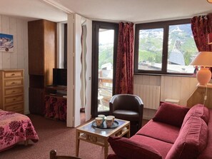 A cozy room with a bed, a sofa, a desk with a chair, and a TV. There is a window with curtains and a view of mountains. - 10m from ski slopes, 3rd floor, balcony, tv, ski locker, 25m², Avoriaz (Avoriaz)