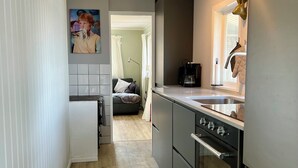 A modern kitchen with a refrigerator, stove, and sink. There is a dining area with a couch and a painting on the wall.