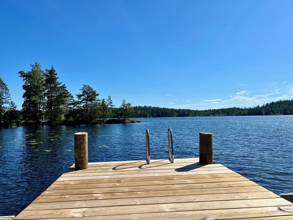 Un muelle de madera se adentra en un lago tranquilo con cielos despejados y una orilla cubierta de bosque.