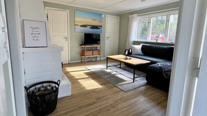 A compact living space with a kitchenette, a sofa, a television, and a window with a view of trees.