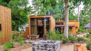 Una cabaña rústica con un hogar a leña de ladrillo, terraza de madera y zona de comedor con mobiliario exterior.