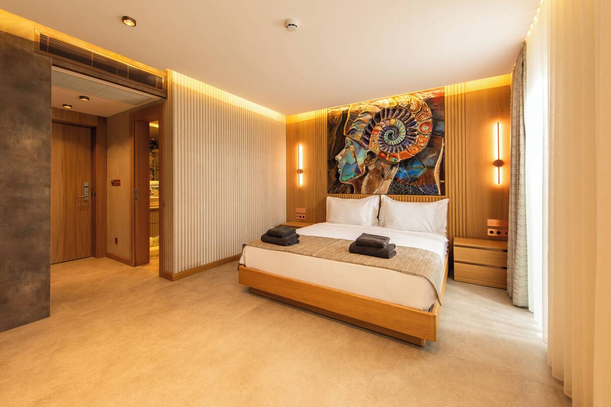 A modern hotel room with a large bed, wooden headboard, and a colorful tapestry.
