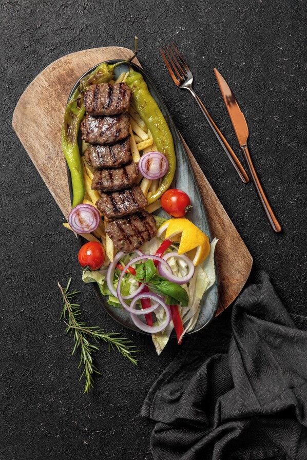 Una comida con carne a la parrilla, papas fritas y verduras sobre una tabla de madera.