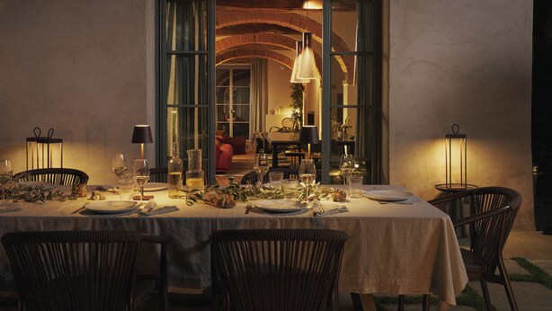A dining area with a table set for a meal, chairs, and a view of a room with a red couch.