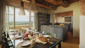 A dining area with a table set for breakfast, a kitchen in the background, and a view of the outdoors.