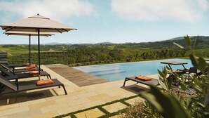 A poolside area with lounge chairs and a table, overlooking a scenic landscape.